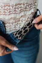 Close-up of a person adjusting a leopard print belt with lace fabric at the top.