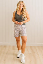 Woman wearing a gray tank top and leopard print shorts standing against a light wooden paneled wall.