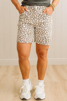 Person wearing leopard print shorts and white sneakers on a plain background