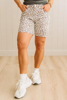 Person wearing leopard print shorts and white sneakers on a wooden floor.