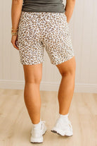 Person wearing leopard print shorts and white sneakers on a plain background