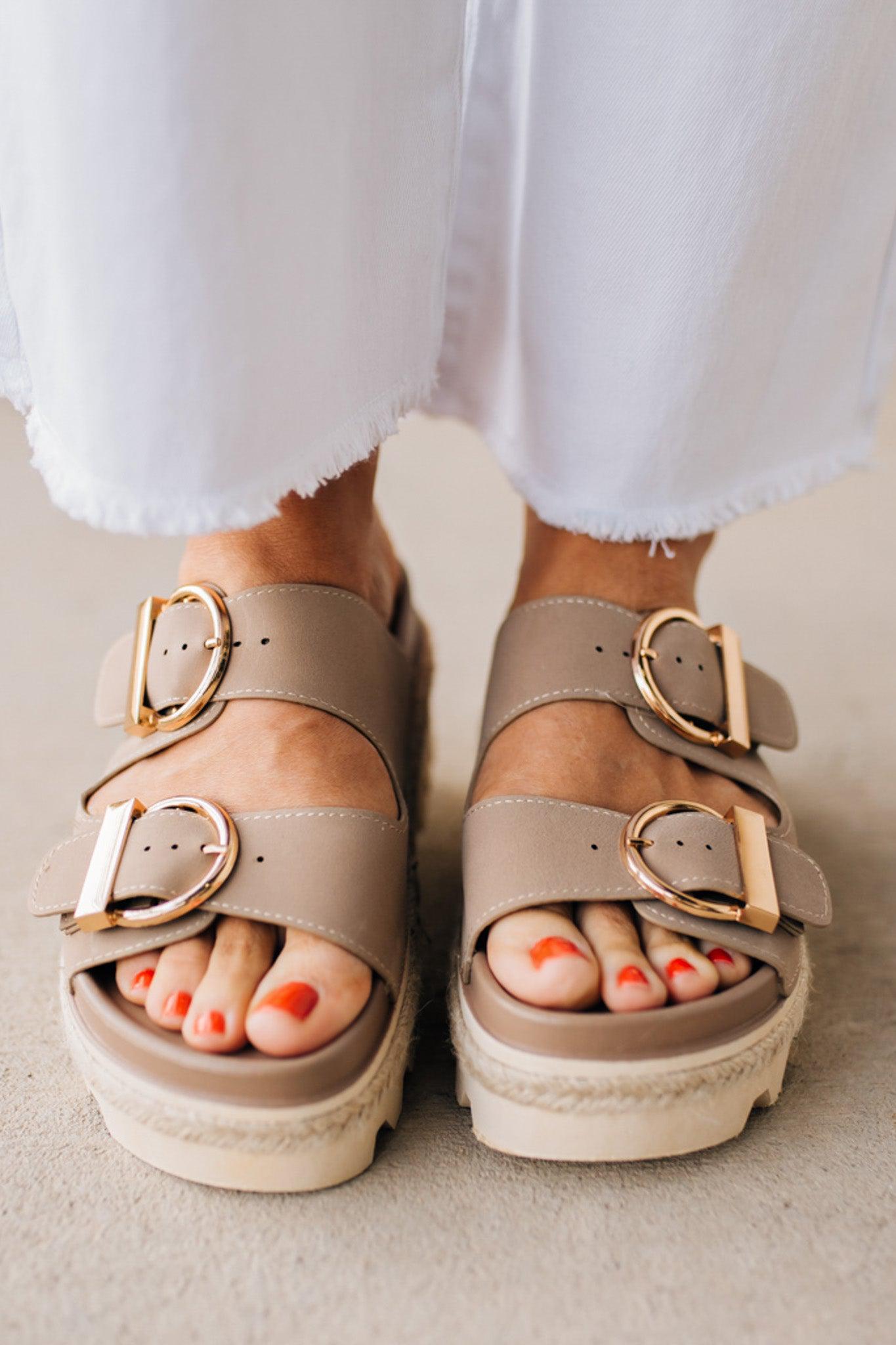 TAUPE PLATFORM SANDAL WITH TWO STRAPS FEATURING A LARGE GOLD BUCKLE ON EACH.