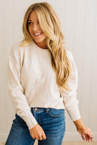 Woman wearing a white sweater and blue jeans against a light background