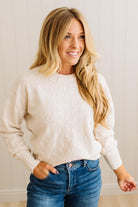 Woman wearing a white sweater and blue jeans against a neutral background