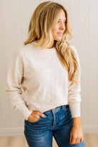 Woman wearing a white sweater and blue jeans against a neutral background