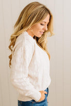 Woman wearing a white cable knit sweater against a plain background