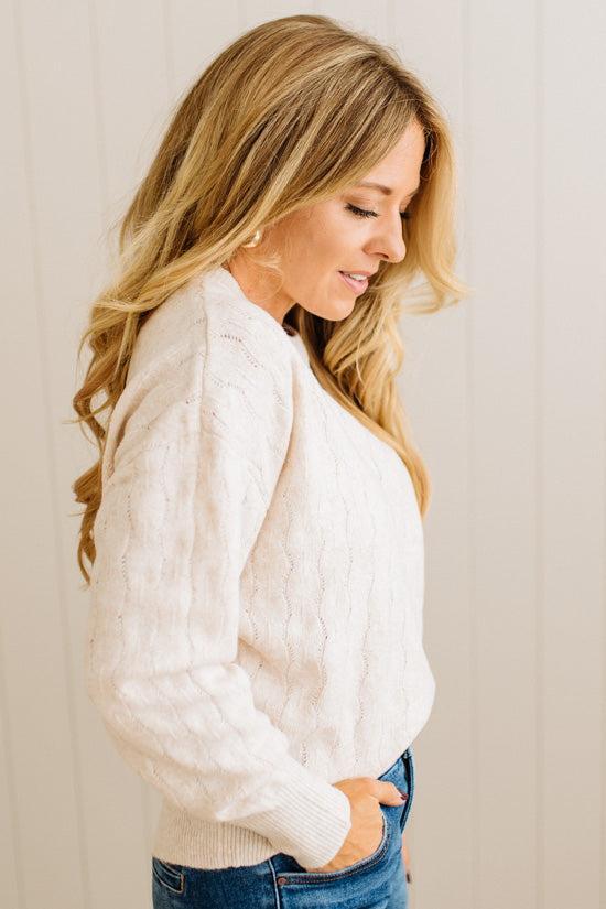 Woman wearing a white cable knit sweater against a plain background