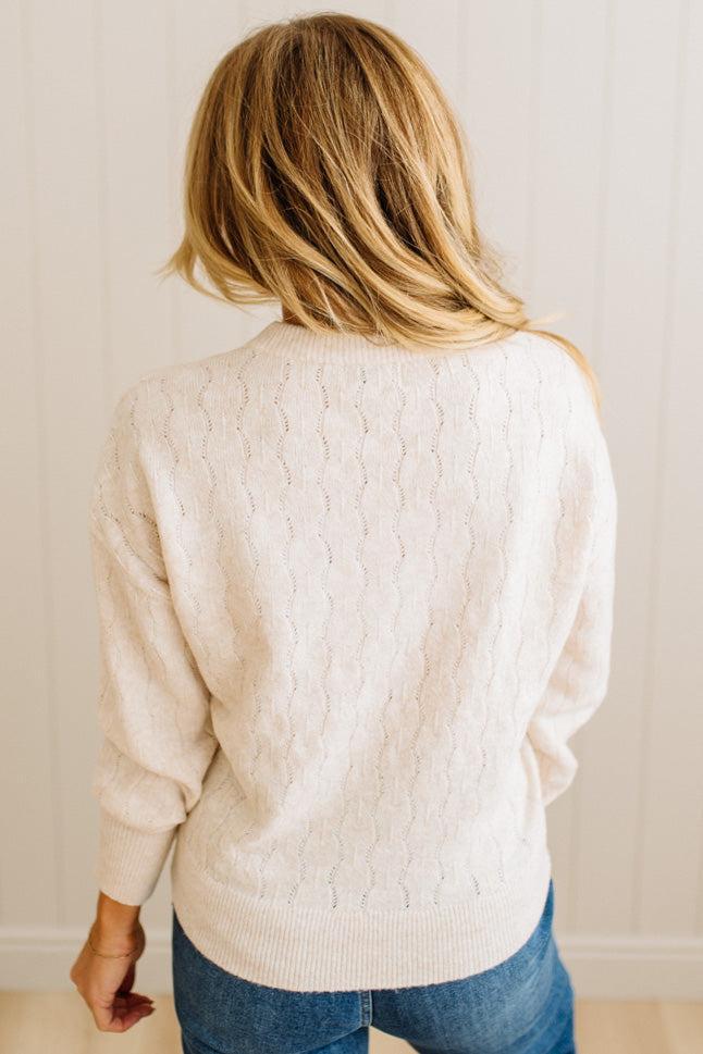 Person wearing a cream sweater and blue jeans against a plain background