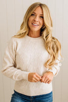 Woman wearing a cream sweater and blue jeans against a white background