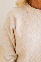 Close-up of a beige cable knit sweater with a neutral background