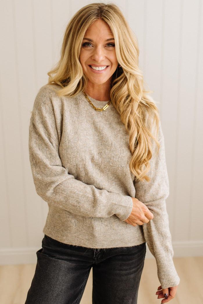 Woman wearing a beige sweater and black pants against a plain background
