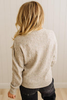 Person wearing a beige sweater and dark pants against a white wall.