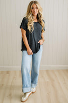 Woman wearing a dark gray t-shirt and light blue jeans standing against a plain wall.