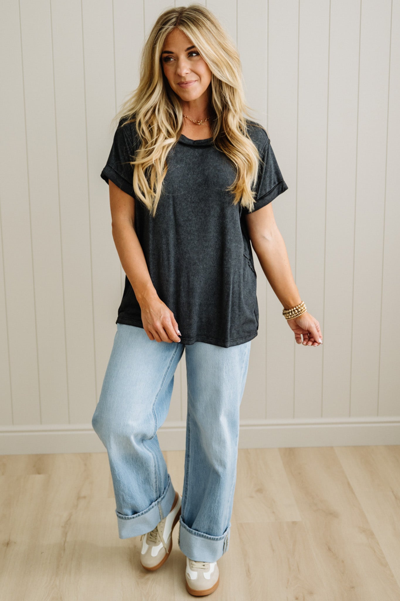 Woman wearing a black t-shirt and light blue jeans standing against a white paneled wall.