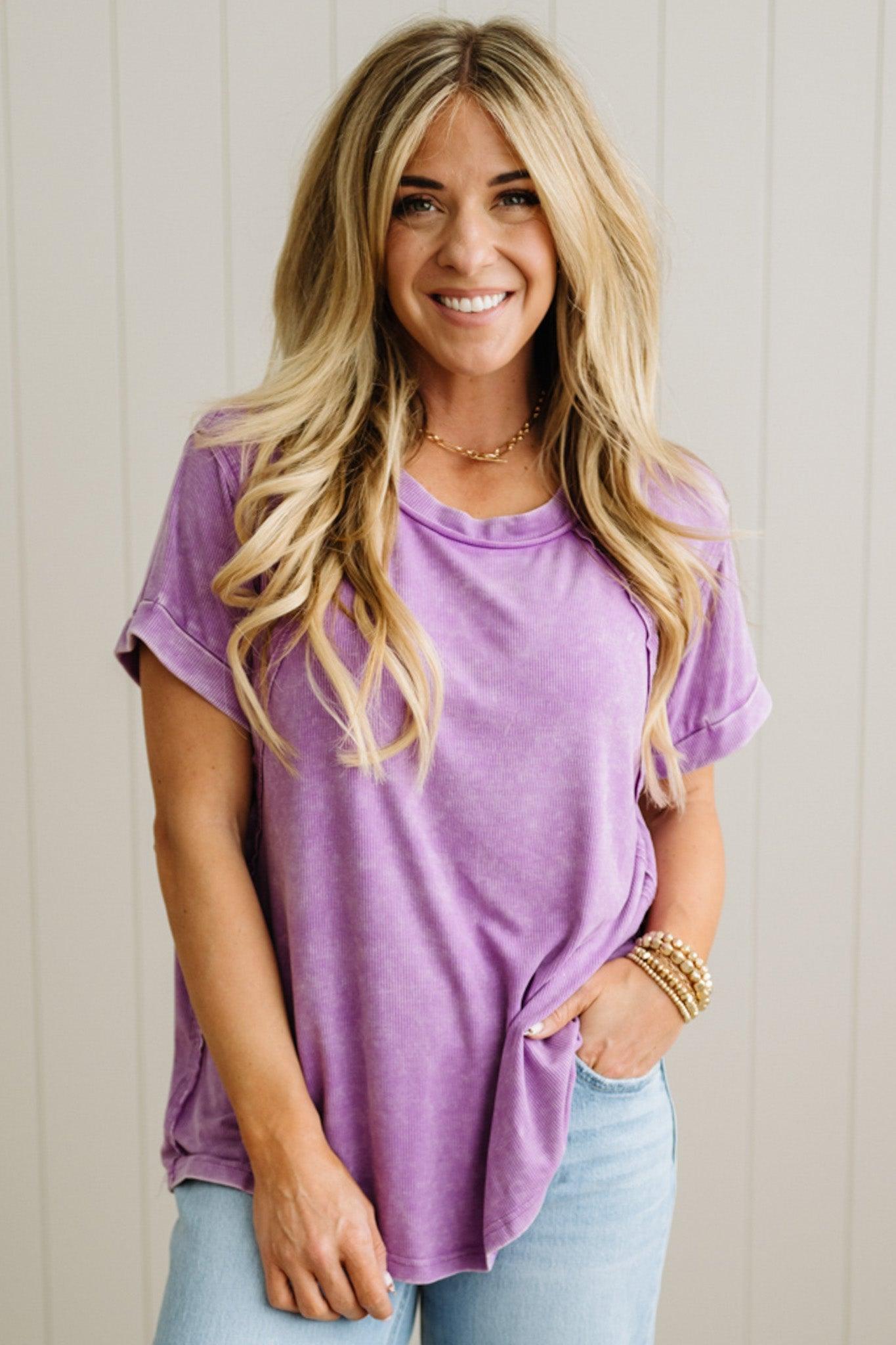Woman wearing a purple t-shirt and light blue jeans against a plain background