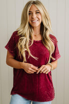 Woman wearing a maroon top and light blue jeans against a neutral background