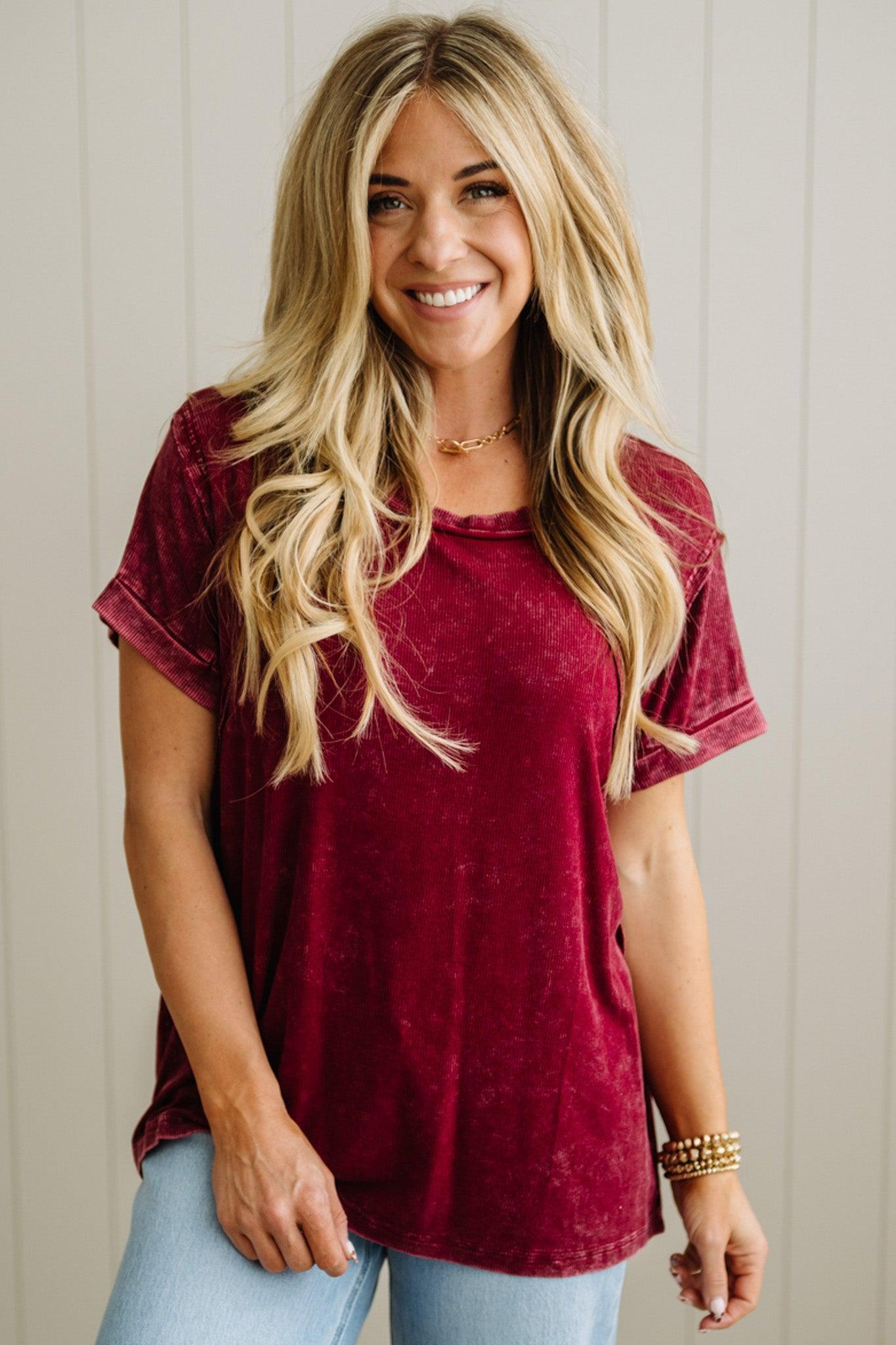 Woman wearing a maroon t-shirt and light blue jeans against a neutral background