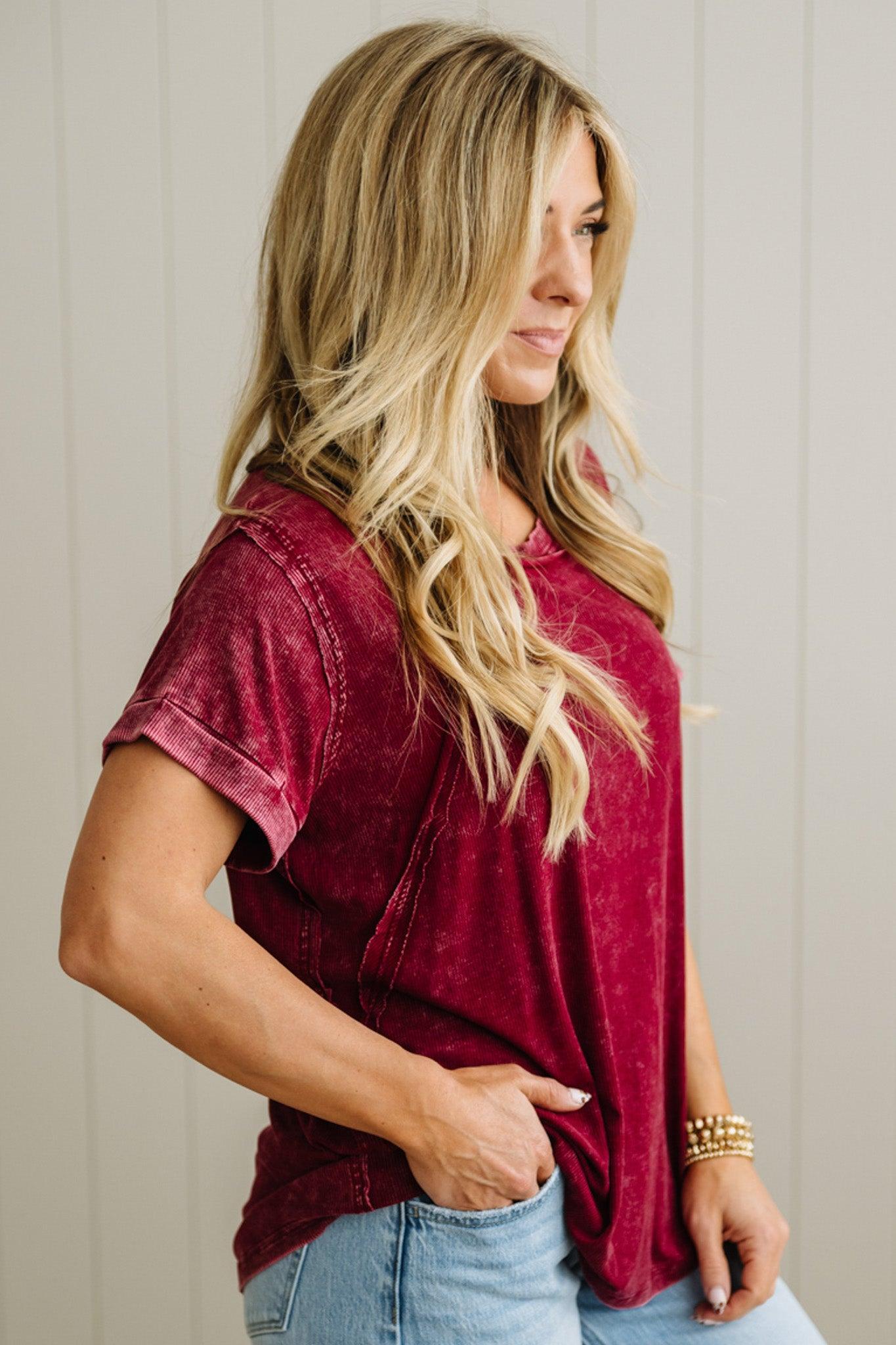 Woman wearing a burgundy t-shirt and blue jeans against a neutral background