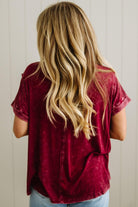Person wearing a maroon shirt with long blonde hair, standing against a neutral background