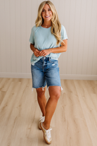 Woman wearing a light blue t-shirt and denim shorts standing on a wooden floor.
