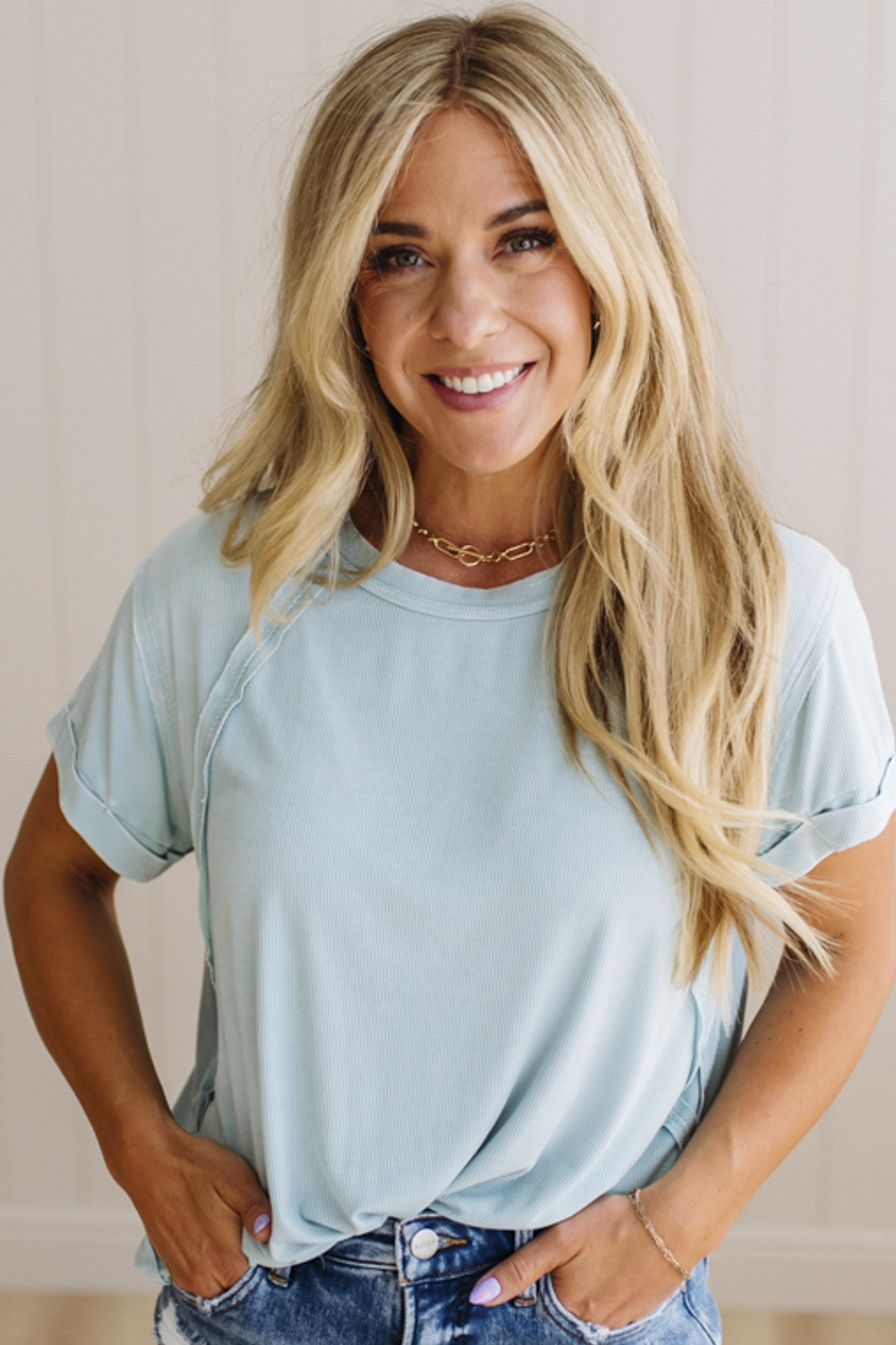 Woman wearing a light blue t-shirt and denim shorts with a neutral background