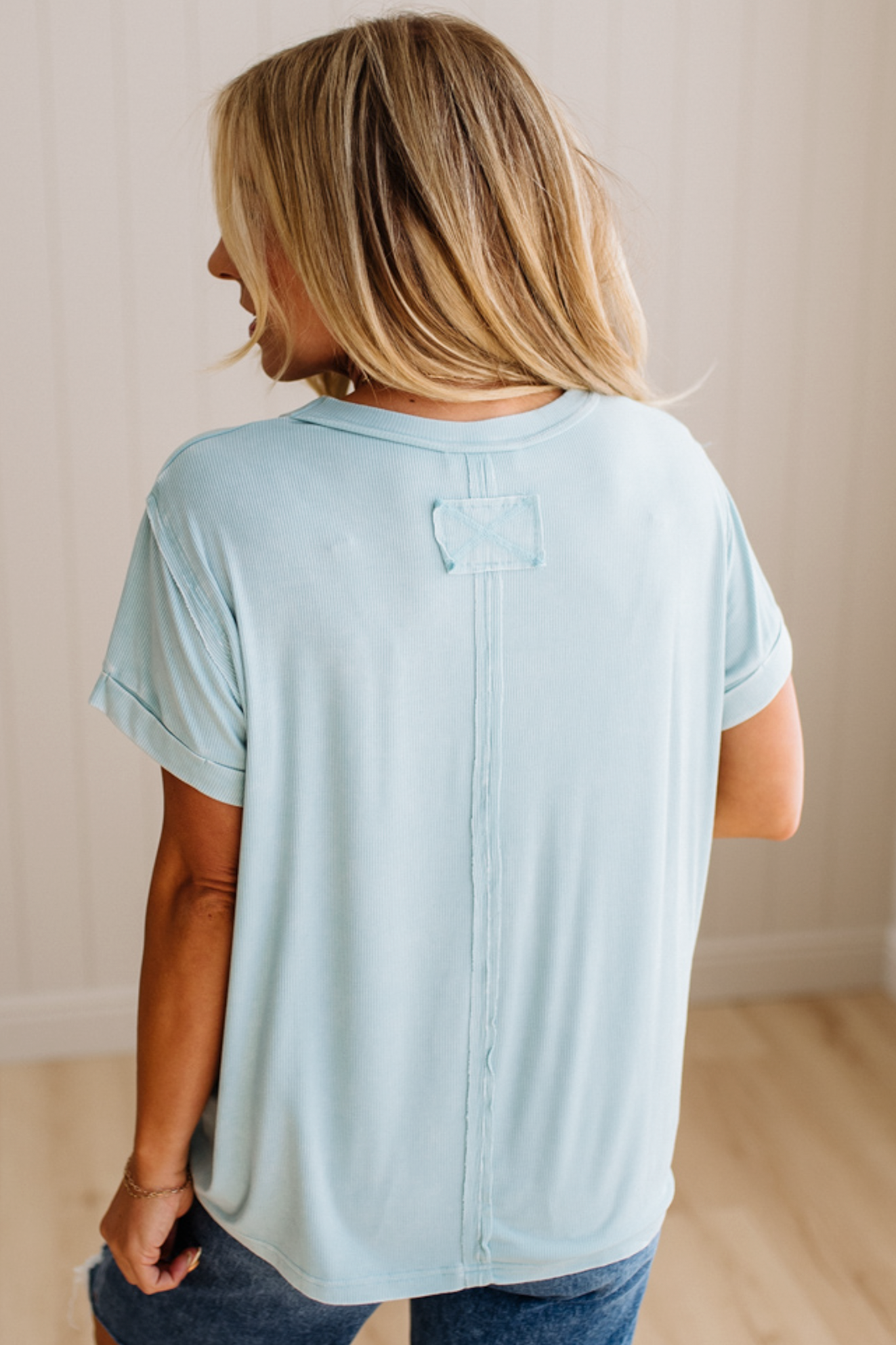 Woman wearing a light blue t-shirt with a subtle pattern, standing indoors.