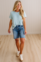 Woman wearing a light blue t-shirt and denim shorts standing on a wooden floor.