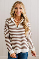 BLONDE WOMAN IN DARK JEANS STANDING IN A BRIGHTLY LIT STUDIO WITH LIGHT WOOD FLOORS AND A PANELED BACKDROP. SHE IS WEARING A CHUNKY NECKLACE AND QUARTER ZIP STRIPES SWEATER IN CREAM AND MOCHA.