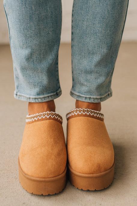 Tan slip-on shoes worn with rolled-up jeans on a neutral background