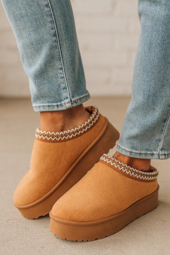 Brown slip-on shoes with patterned socks worn with light blue jeans on a neutral background