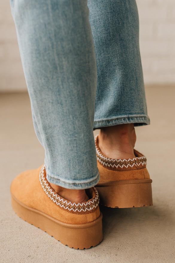 Brown platform shoes with white stitching worn with light blue jeans on a neutral background