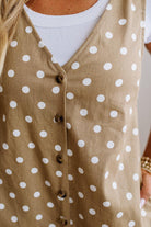 A close-up of a woman wearing a sleeveless tan vest with white polka dots and dark brown buttons over a white ribbed top.