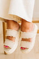 White sandals with ruffled details worn by a person sitting on a chair.