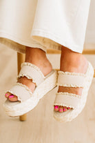 White lace sandals worn with a white dress on a neutral background