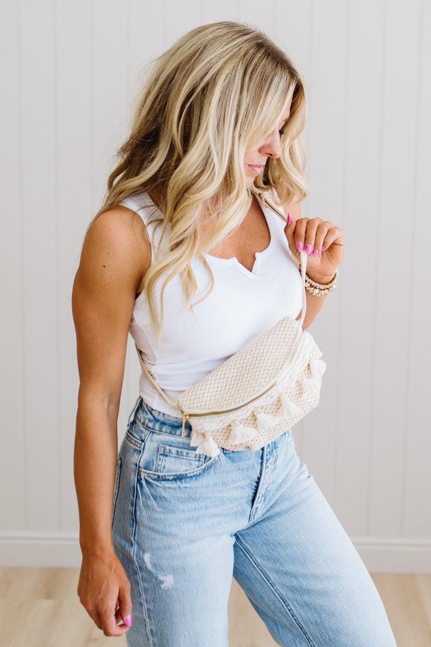 Woman wearing a white sleeveless top and light blue jeans with a beige waist bag.