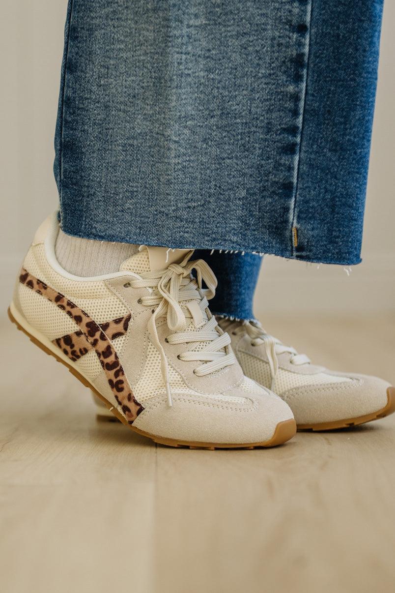 White sneakers with leopard print details worn with blue jeans on a neutral background