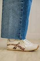 White sneakers with leopard print details worn with blue jeans on a neutral background