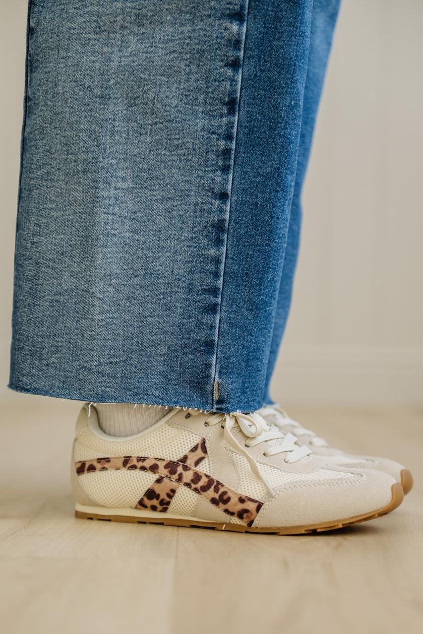 White sneakers with leopard print details worn with blue jeans on a neutral background