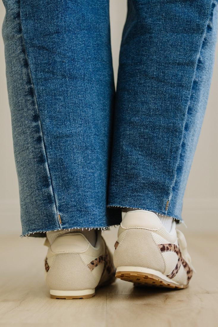 Close-up of blue jeans and beige sneakers on a neutral background
