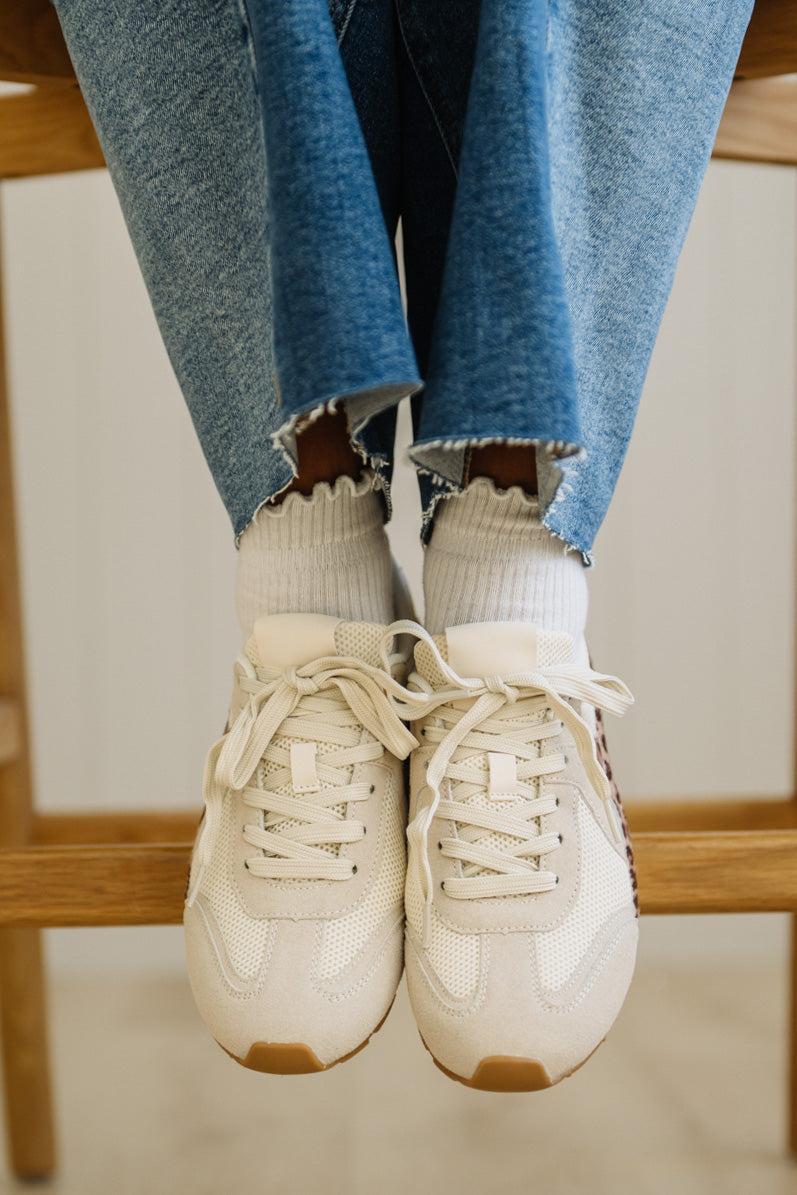 White sneakers with brown accents worn with blue jeans and white socks.