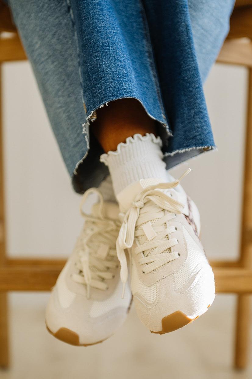 White sneakers with brown accents worn with blue jeans and white socks.