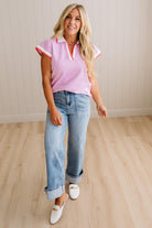 Woman wearing a pink sleeveless top with white trim and blue jeans indoors.