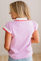 Woman wearing a pink polo shirt with white trim against a neutral background