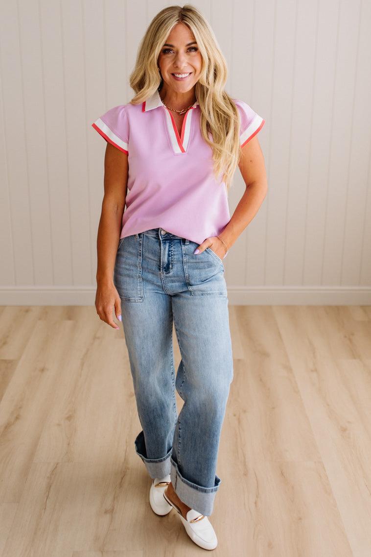 Woman wearing a pink and white striped shirt with blue jeans on a wooden floor.