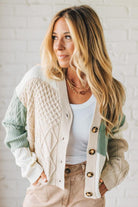 Woman wearing a cable knit cardigan with a white brick wall background