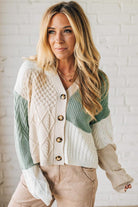Woman wearing a green and beige cardigan against a white brick wall