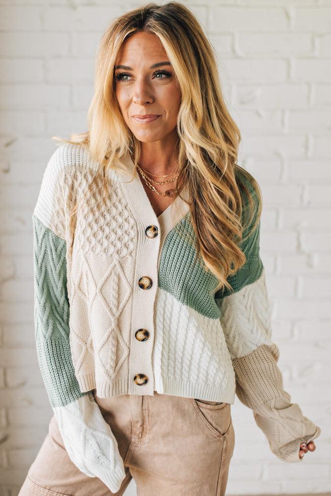 Woman wearing a green and beige cardigan against a white brick wall