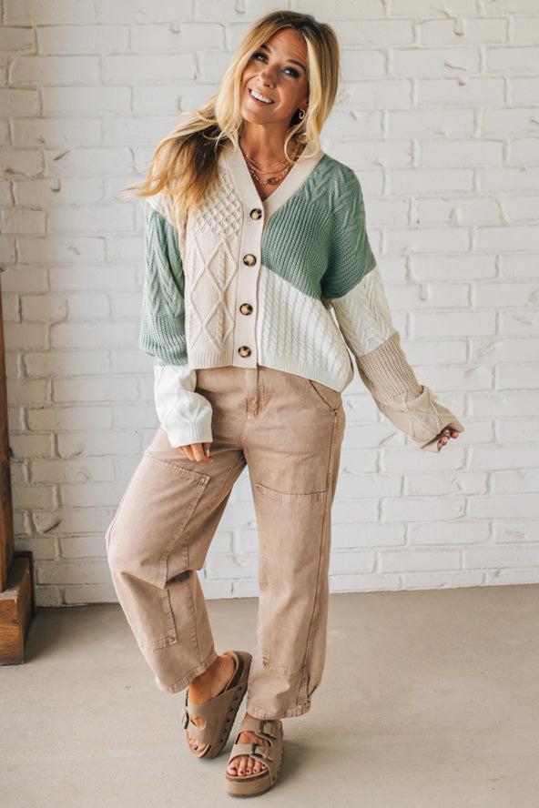 Woman wearing a color-blocked cardigan and beige pants against a white brick wall.