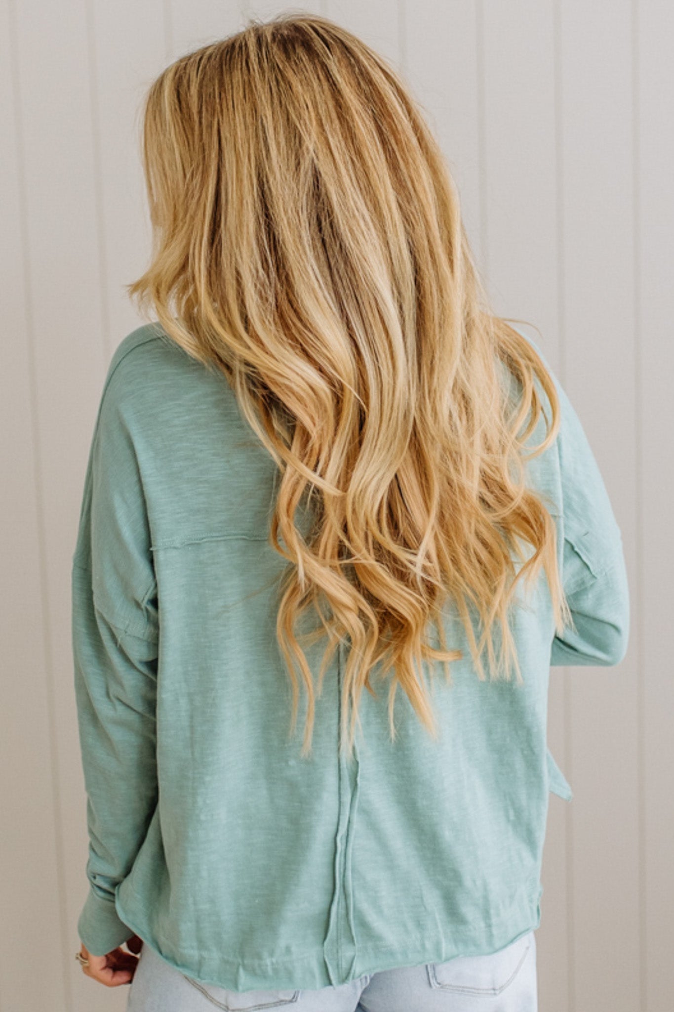 Person wearing a light green shirt with long blonde hair, standing against a neutral background