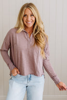 Woman wearing a mauve long-sleeve shirt and light blue jeans against a white paneled wall.